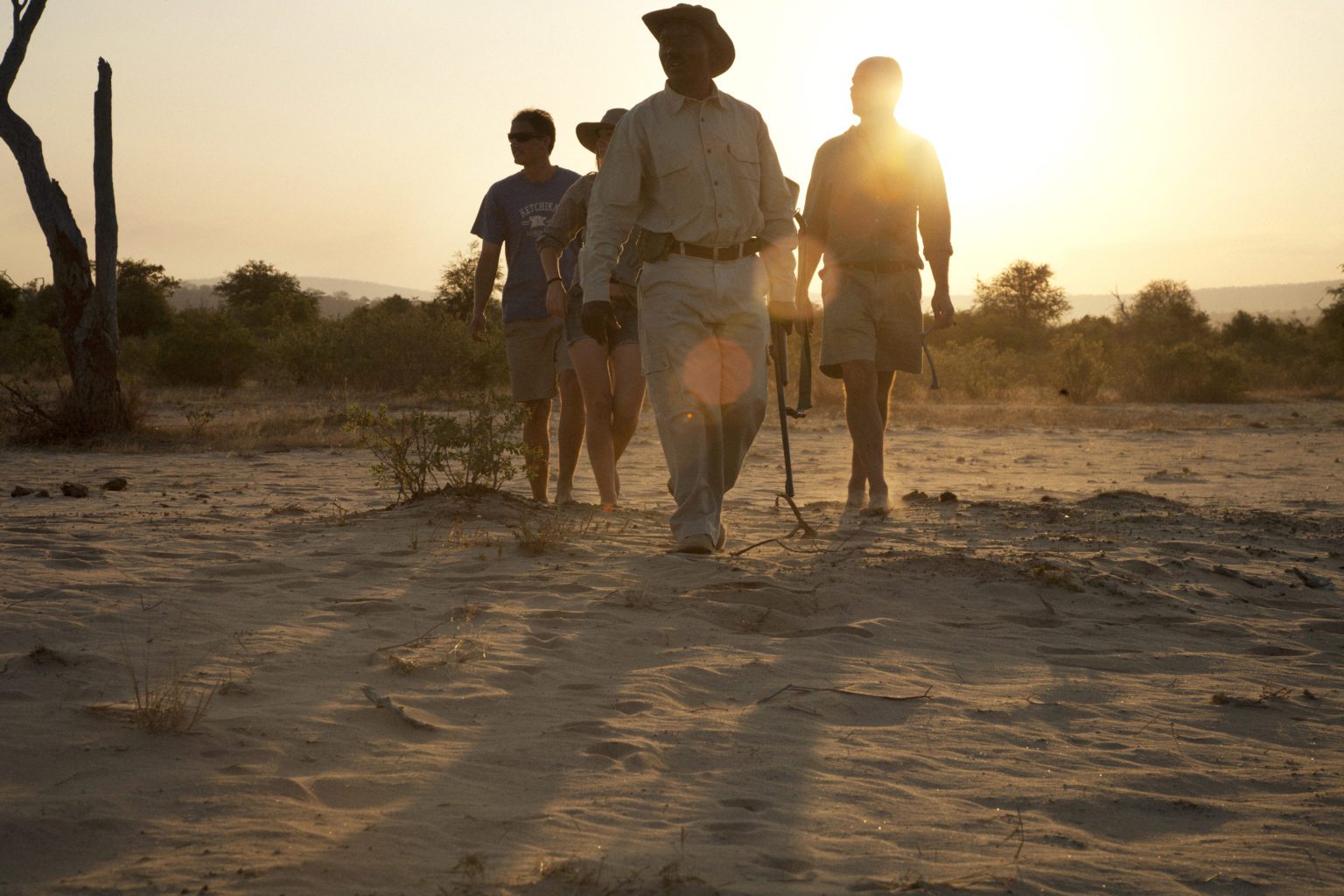 guests walking in the sand at sunrise with and armed ranger