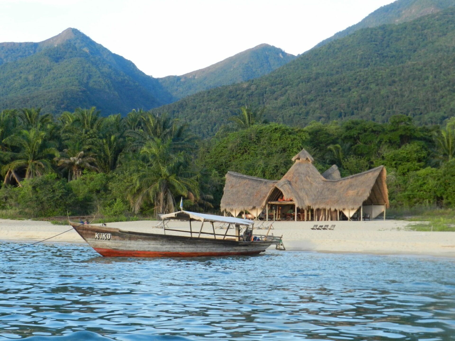 dhow boat in the water in front of Greystoke's main lodge with Mahale Mountains behind