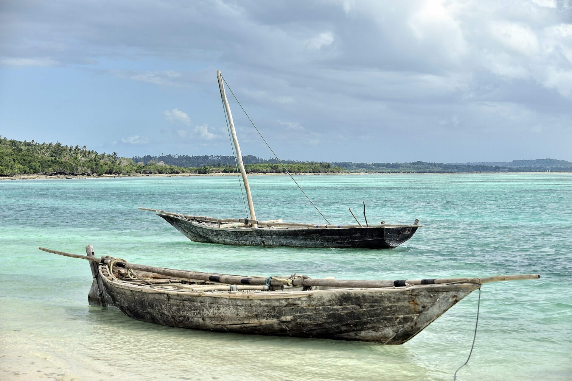 two fishing dhows in turquoise water on white sandy beach