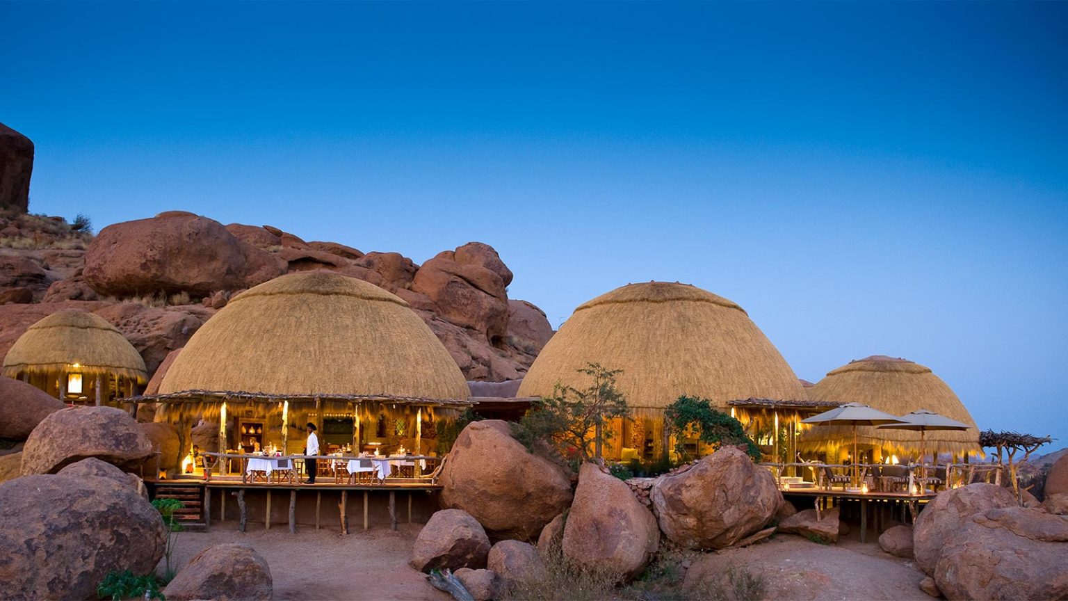 on our best Namibia safari you'll see domed thatch roofs of Camp Kipwe at sunset