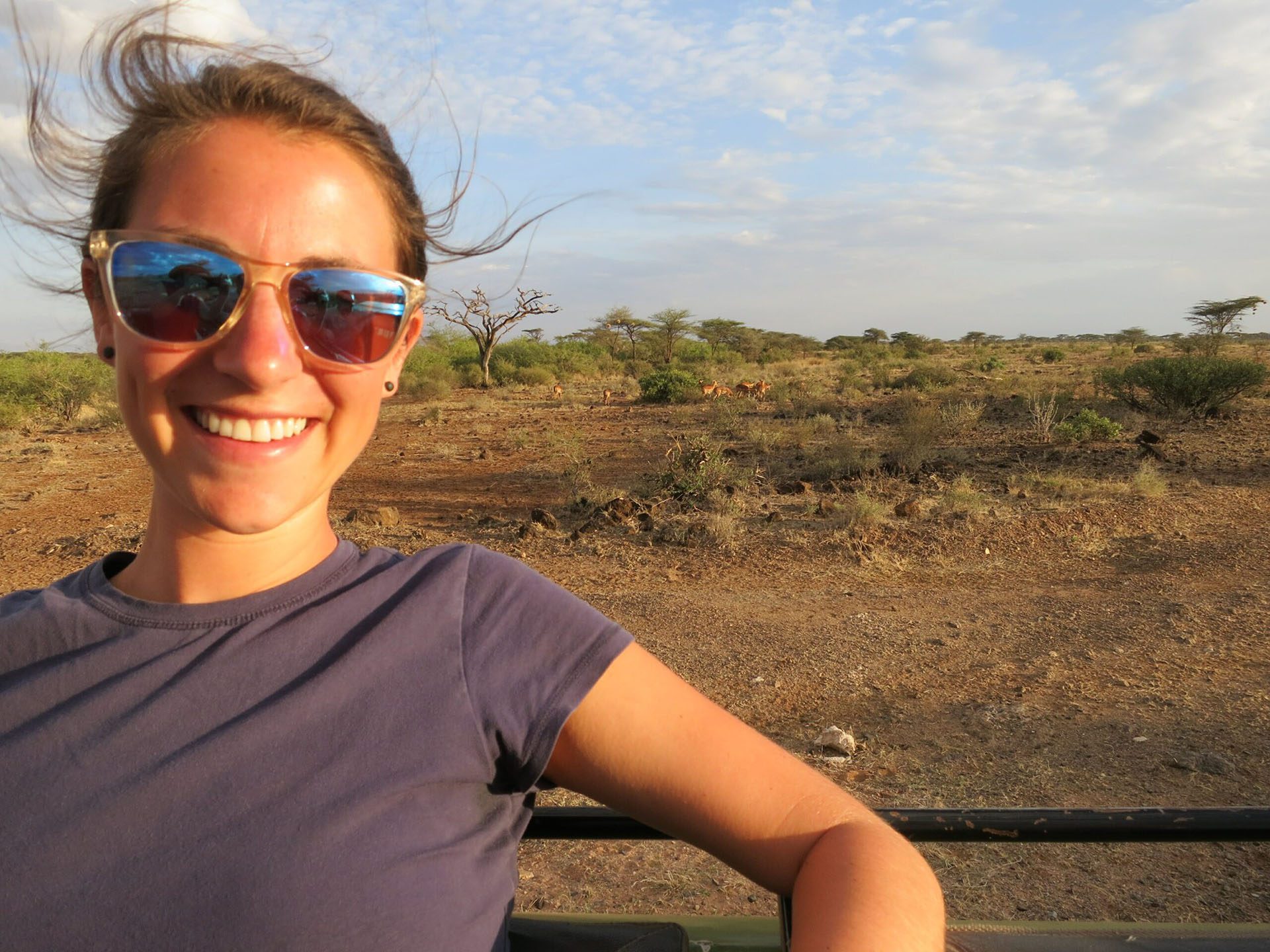 a woman wearing sunglasses and smiling in front of a field.