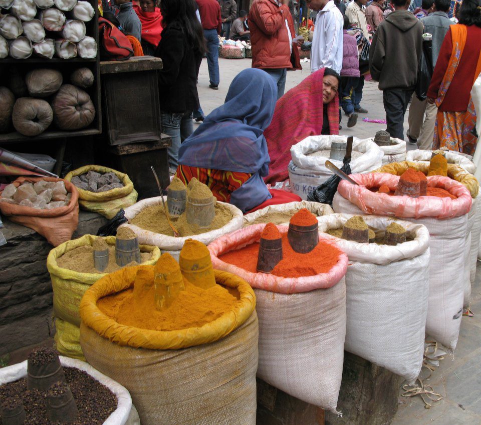 two women talking behind rows of colorful spices in a market in Kathmandu, Nepal