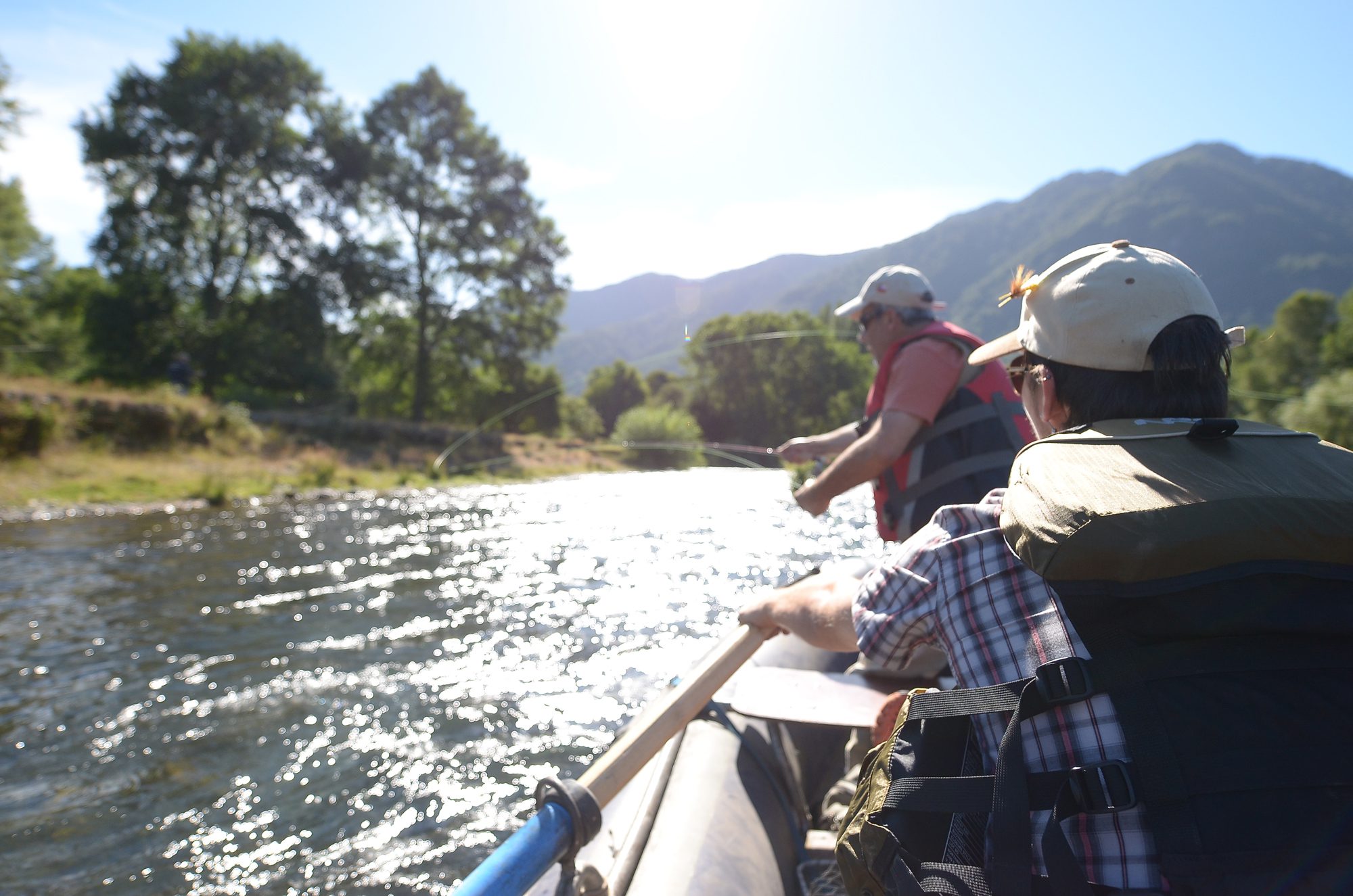 Group of travelers in boat, fishing along river in Lake District surrounded by trees and mountains