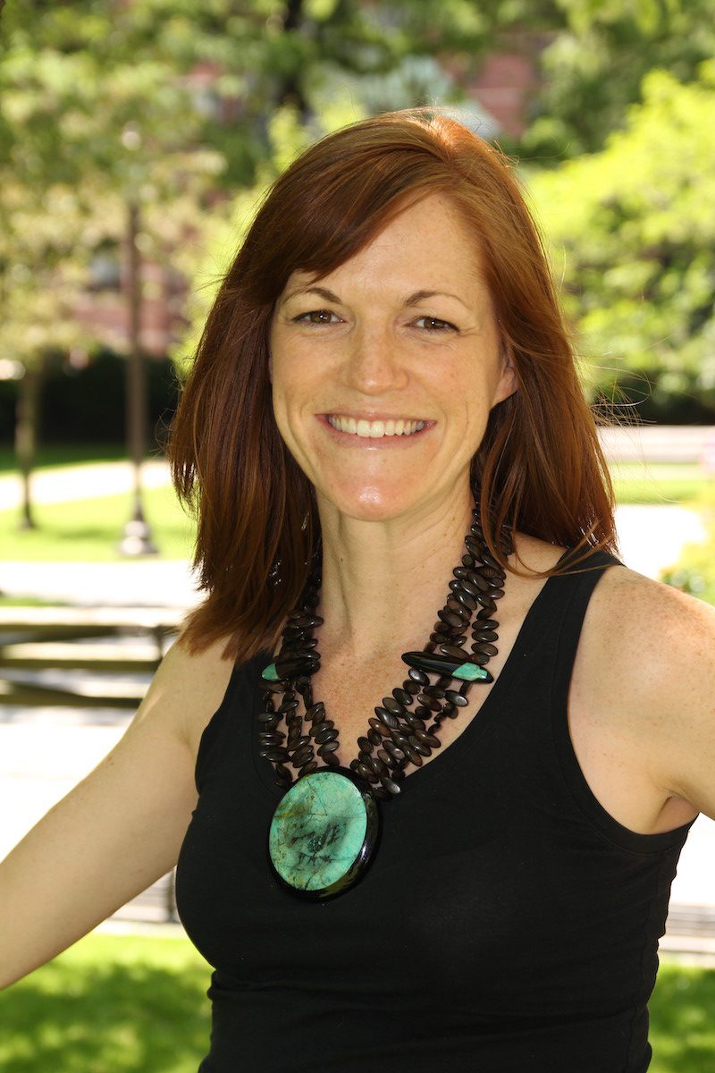 a woman wearing a black top and a green necklace.