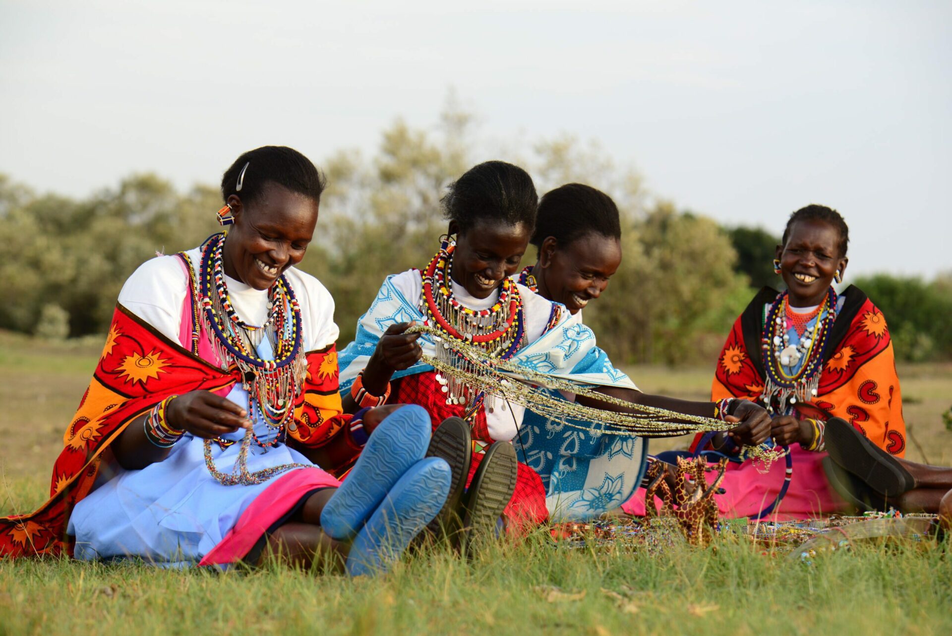 group of brightly dressed Maasai women beading while sitting in the grass