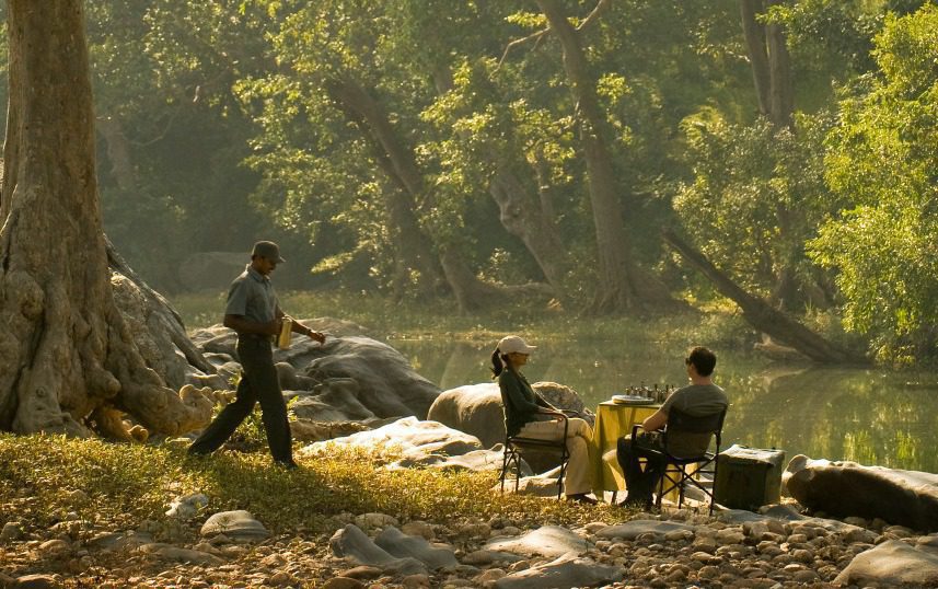 two people sitting in chairs overlooking a river with a guide walking toward them