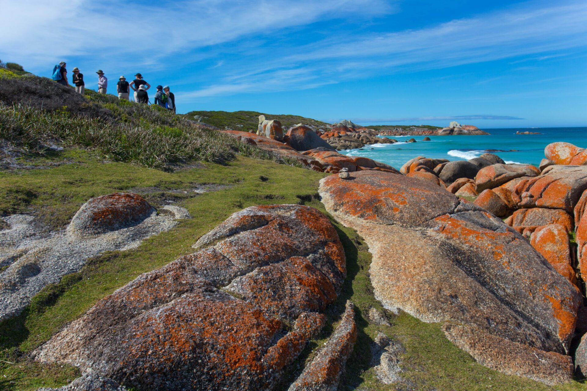 people walking in the distance with lichen covered rocks and beach in the foreground on a hiking and climbing safari