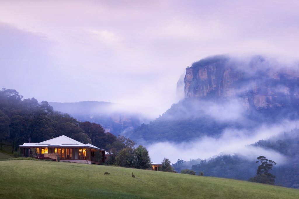 Emirates Wolgan Valley in the Blue Mountains, an isolated building on a misty hillside with mountains in the background.