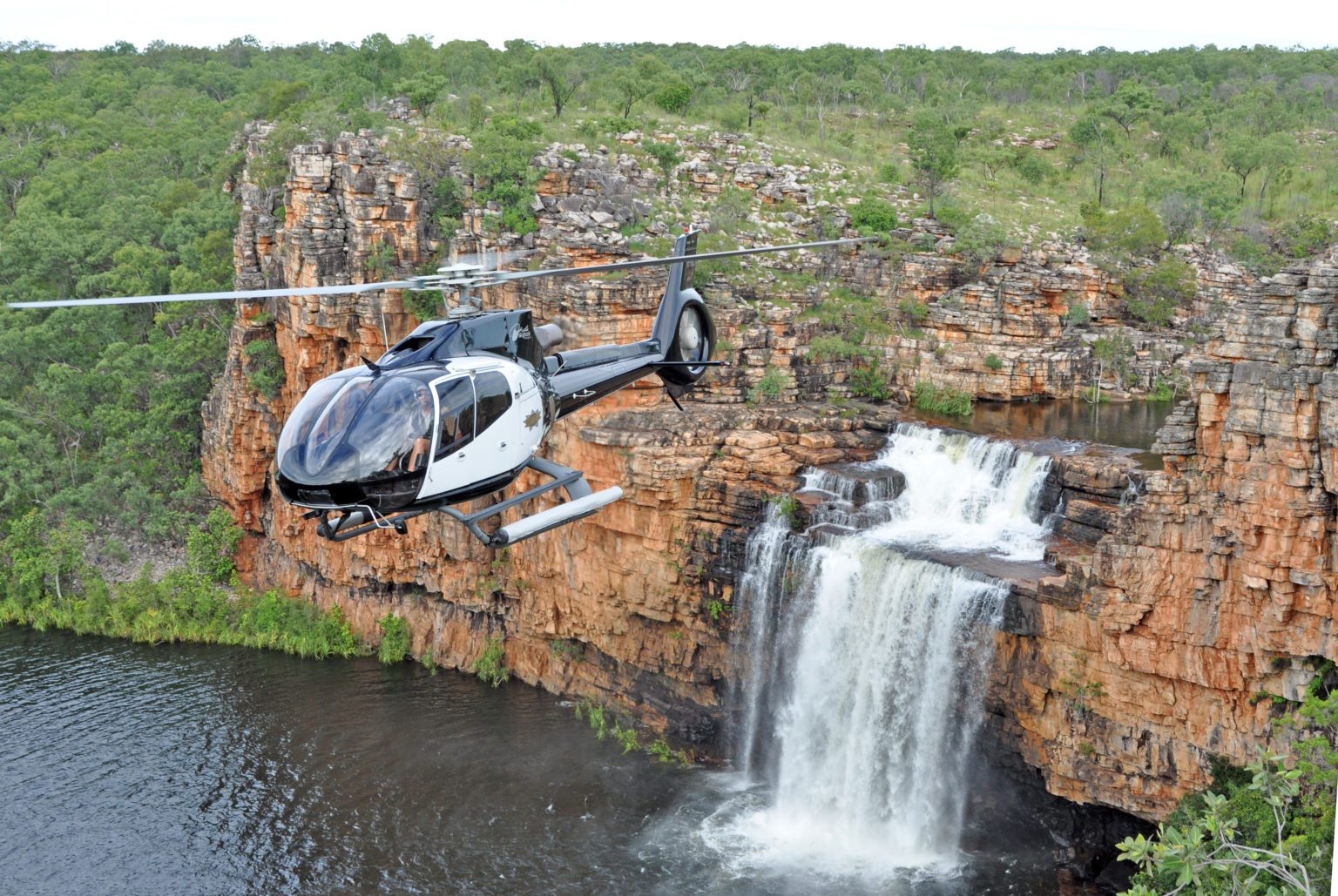 A helicopter flies above a waterfall in Kimberley