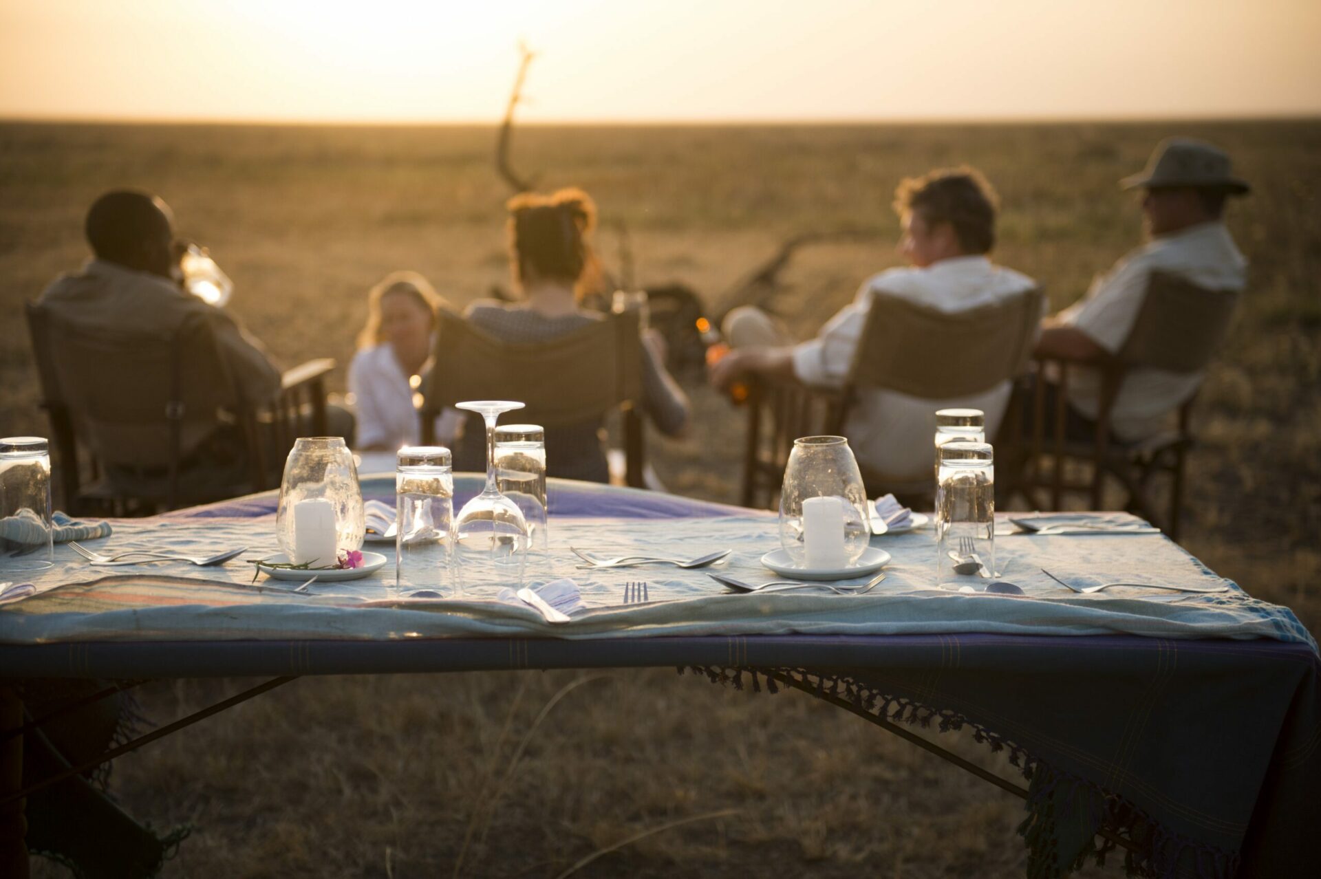 table set up outside with guests sitting in chairs looking out onto the open plains at sunset