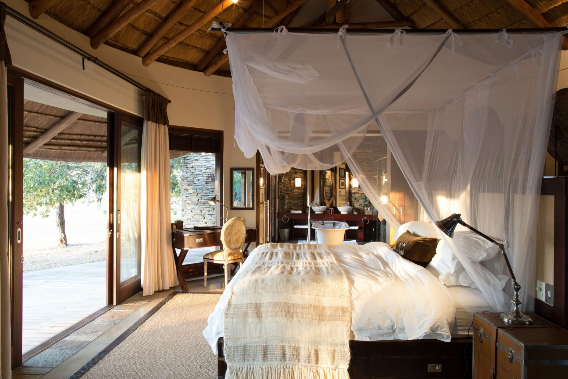 bed draped with mosquito net looking out to the bush at makanyi lodge on this South Africa and Namibia safari