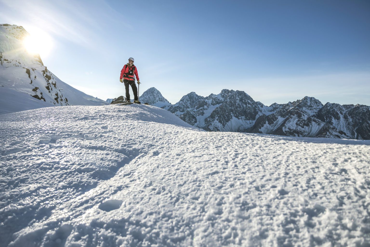 A lone climbers on a snowy mountaintop with more peaks in the background.
