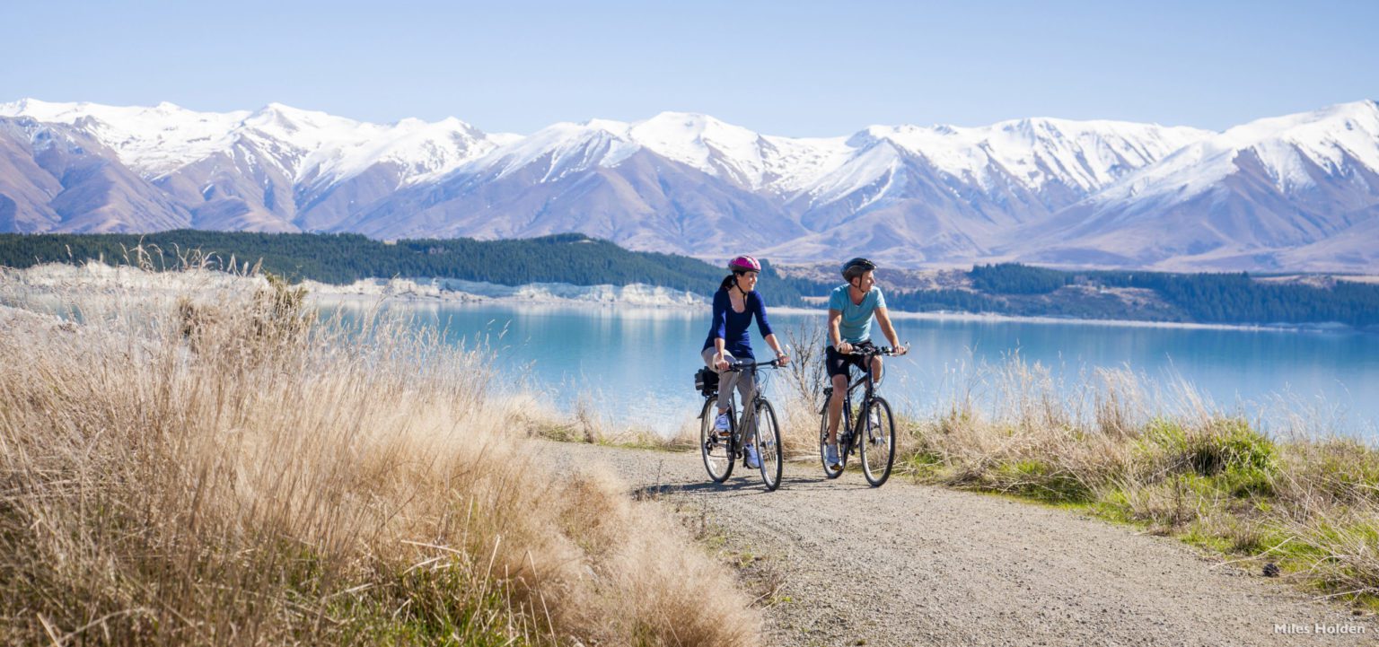 Two cyclists biking along Lake Pukaki with the Southern Alps in the background on New Zealand's South Island tour
