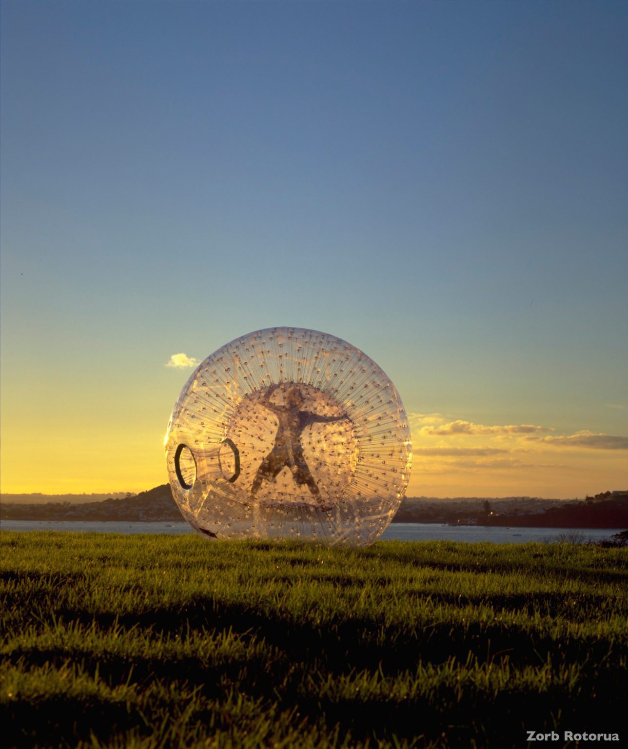 A person in a star-position Zorbing down a hill at dusk