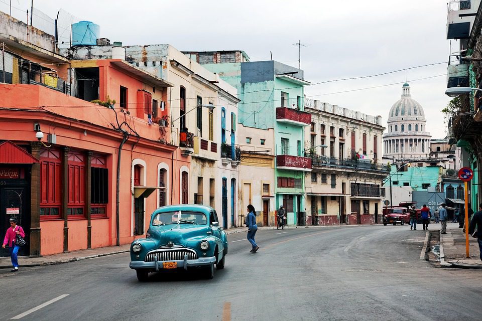 Classic blue automobile driving past worn buildings in Havana