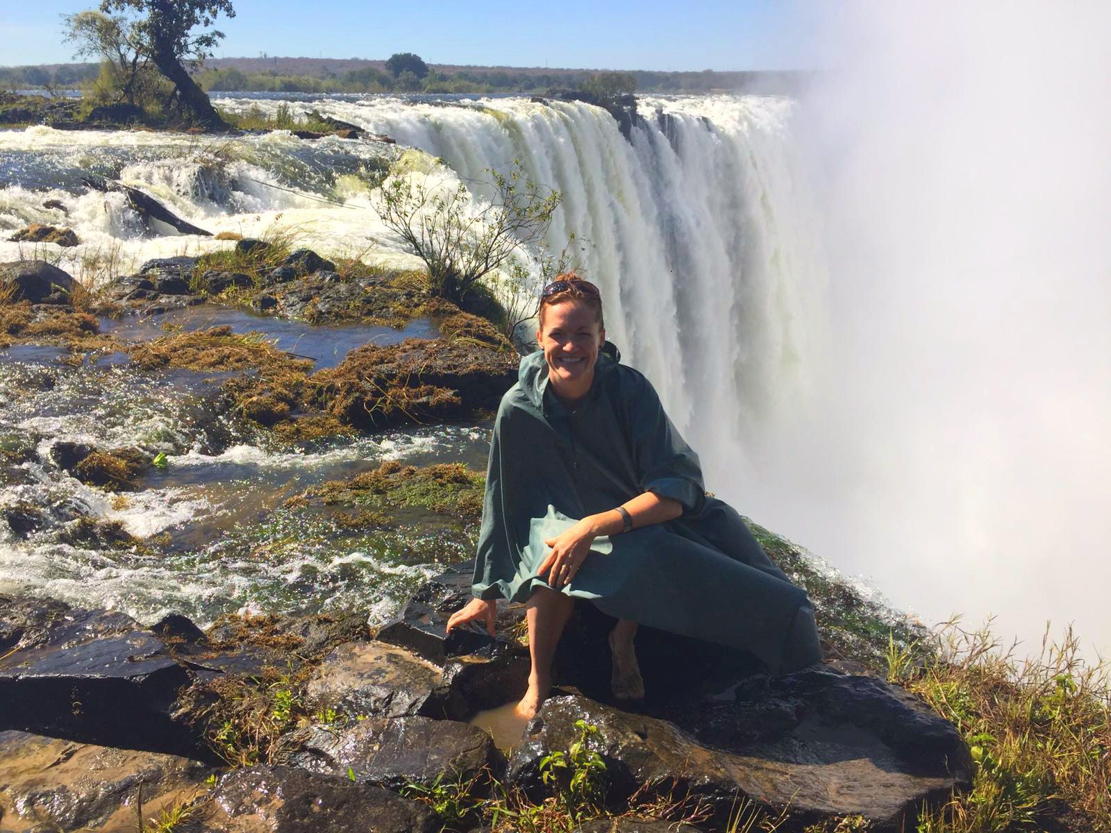 woman sitting by the edge of victoria falls in a poncho on this Southern Africa safari