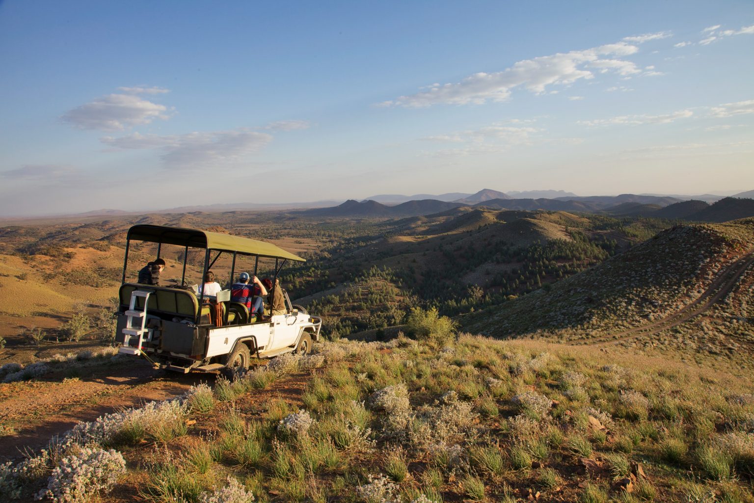 A safari vehicle driving on a dirt road through the hills of the Flinders Ranges at Arkaba