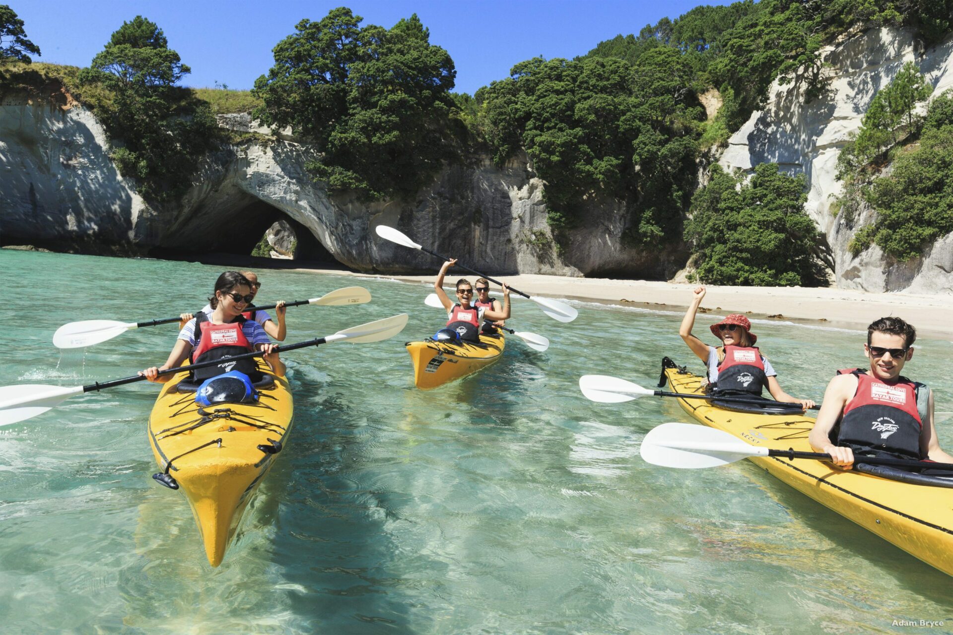 A group kayaking in the clear waters below some cliff faces in Coromandel.
