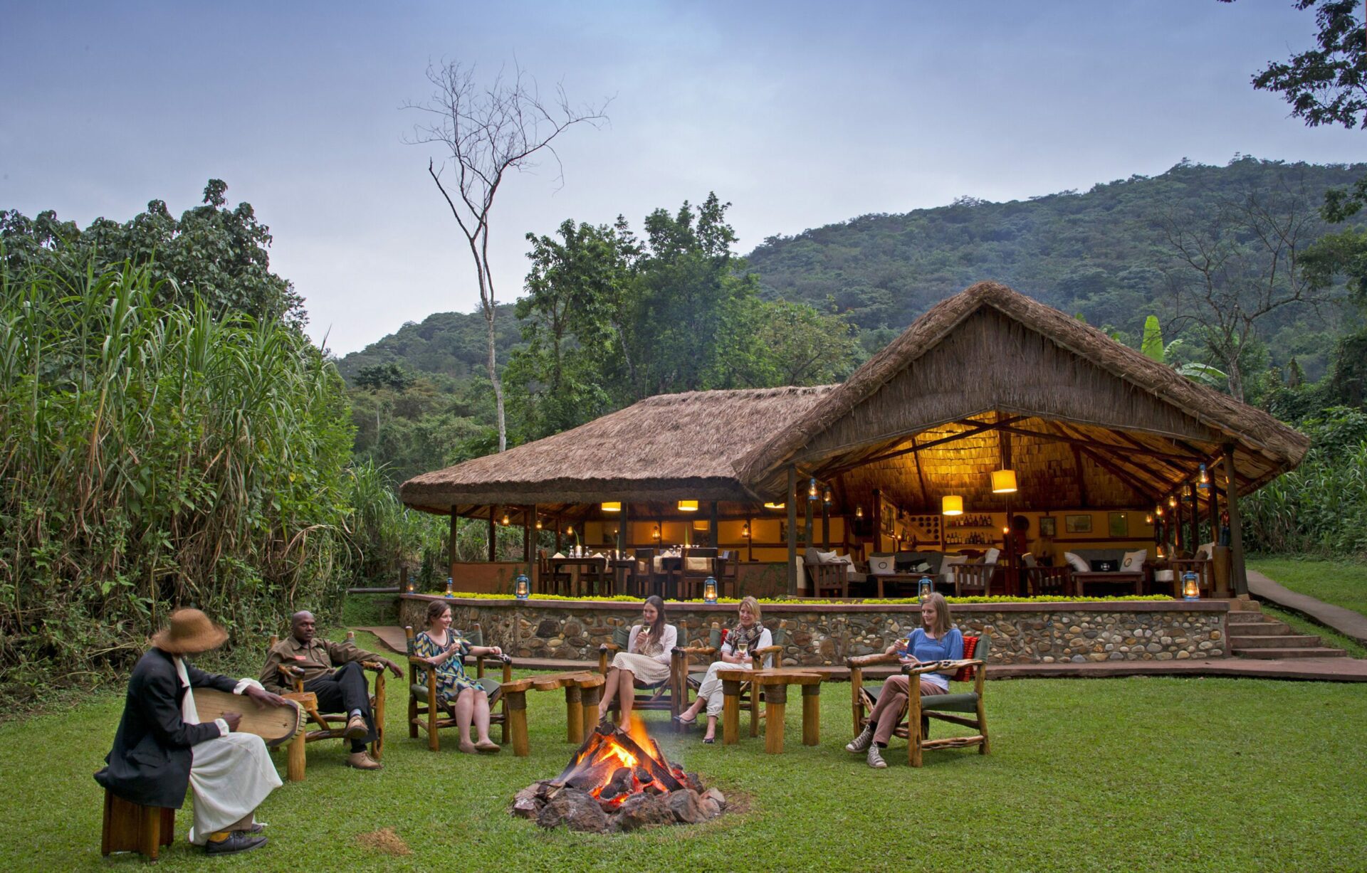 guests enjoying a drink around the campfire in front of the main lounge at Gorilla Forest Camp tucked into the forest on East Africa safari