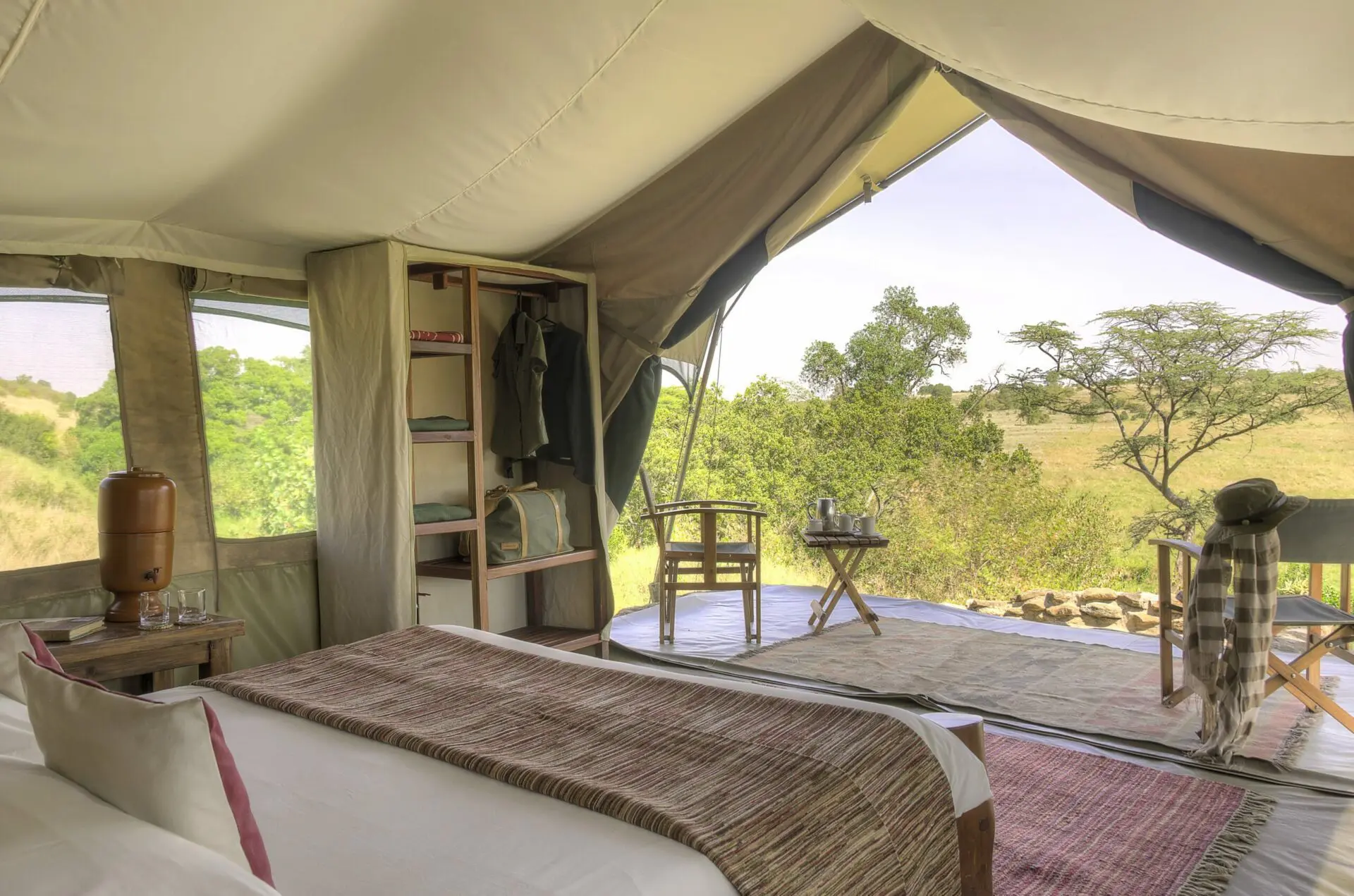 interior view of a tent at Kicheche Mara with a bed, vanity, and chairs overlooking the bush