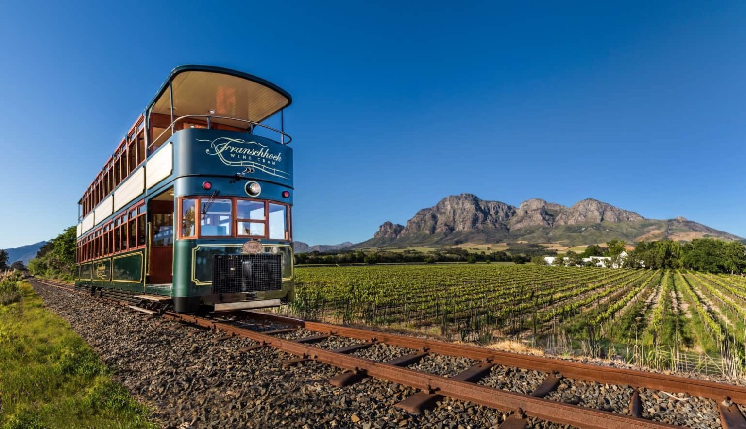 tram on railroad tracks going past vineyards and mountains on a clear day on a Africa food and wine safari