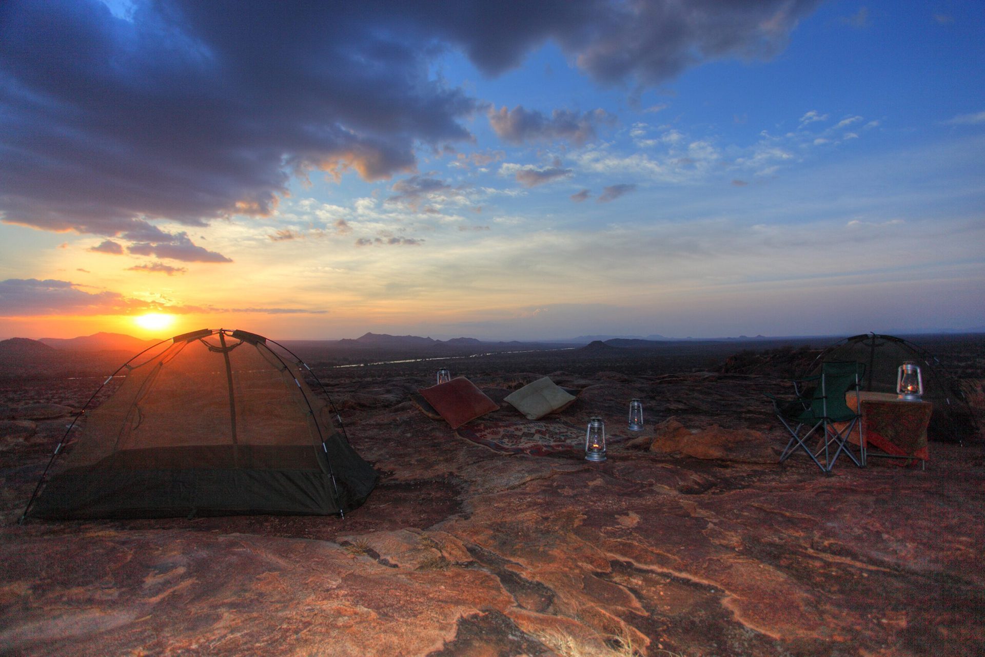 a tent set up on a rocky outcropping with the sun setting in.