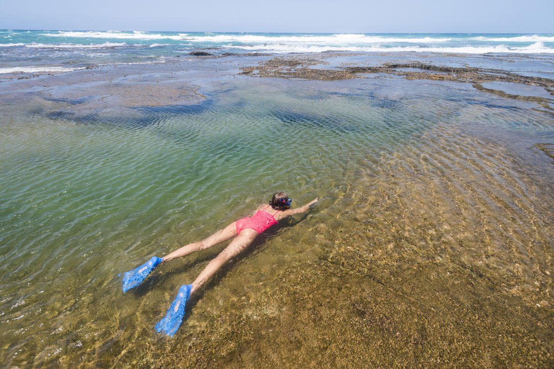 Person wear pink swim suit snorkeling in shallow ocean water.