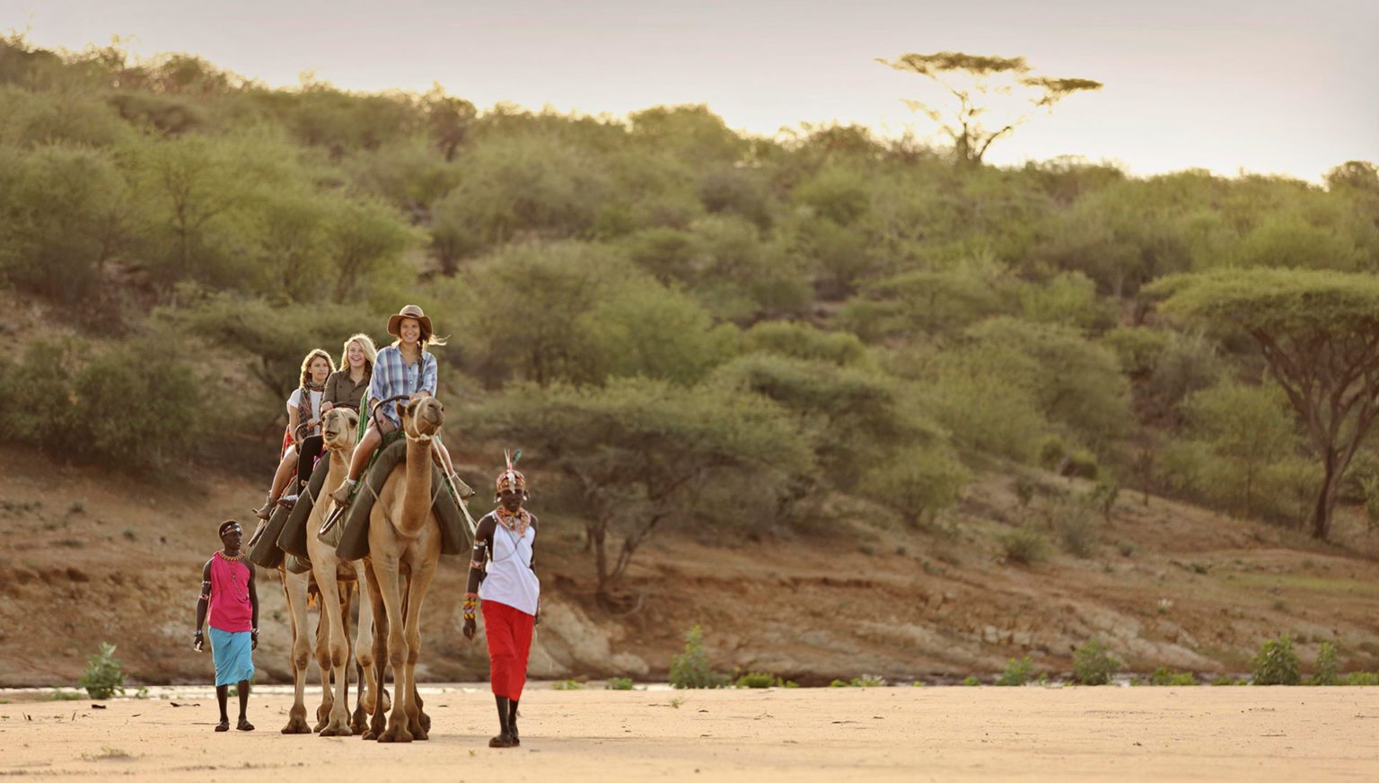 family on top of camels being led across a dry river by a Samburu on our best East Africa safari