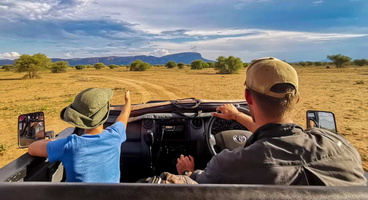 child spotting wildlife on a game drive, sitting beside a ranger