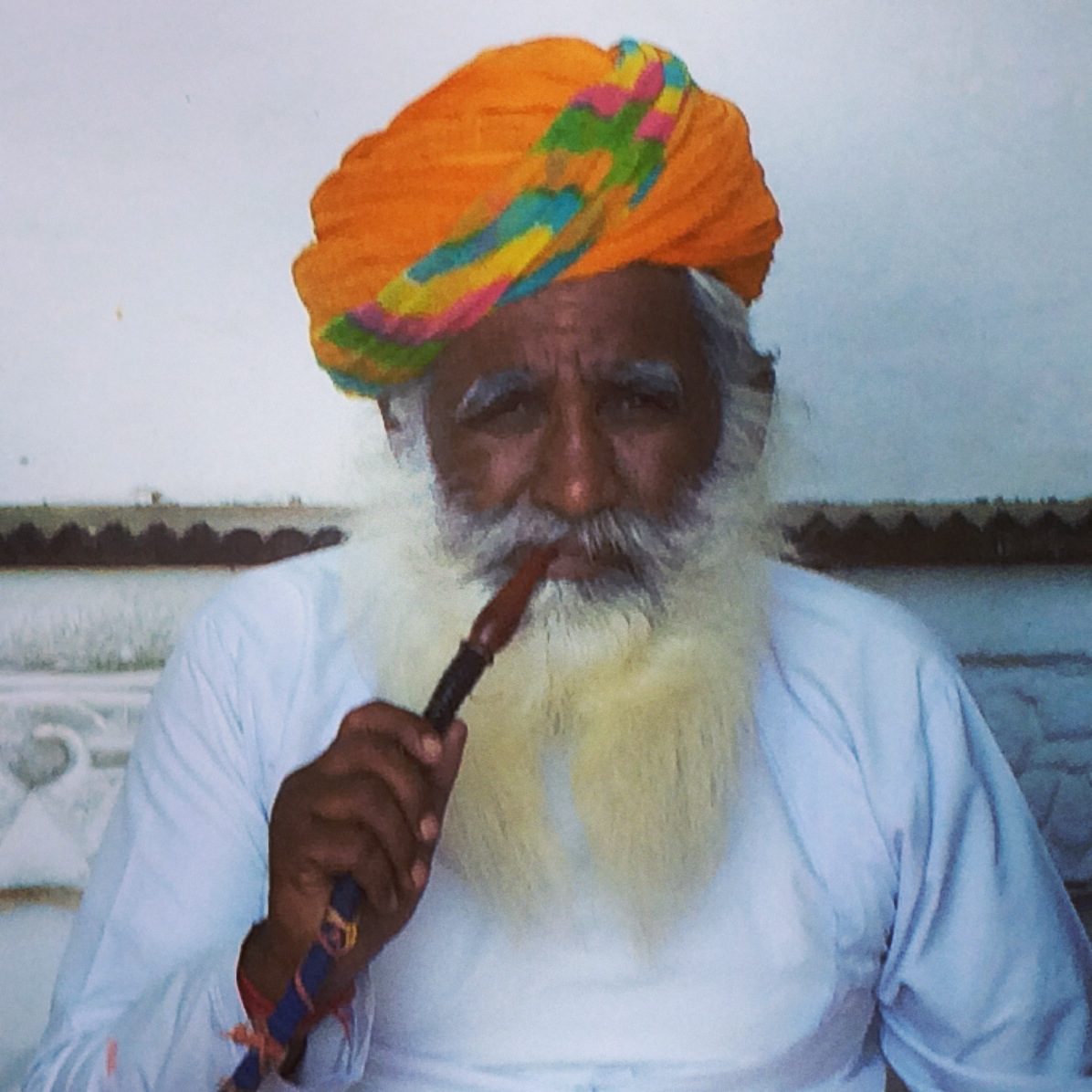 old man with a yellowish beard and orange turban smoking a hookah pipe