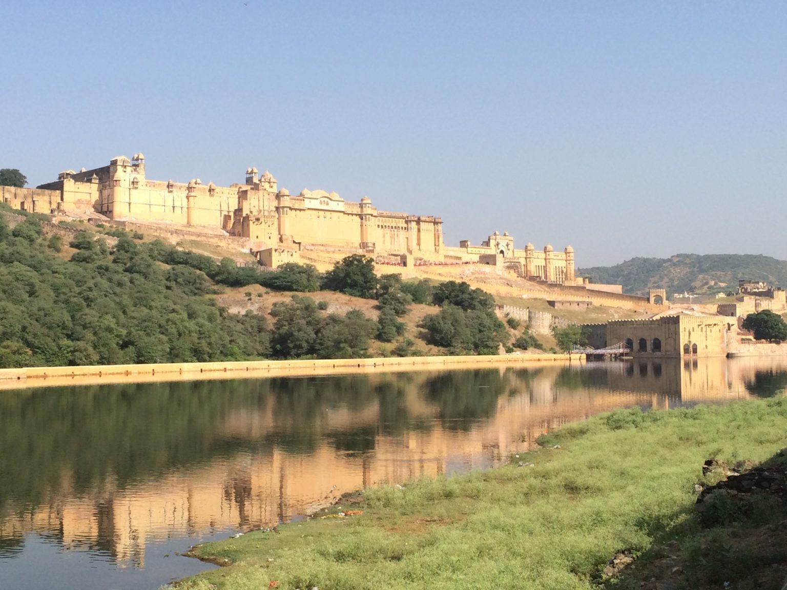 Amber Fort seen from a distance over some grass and a river.