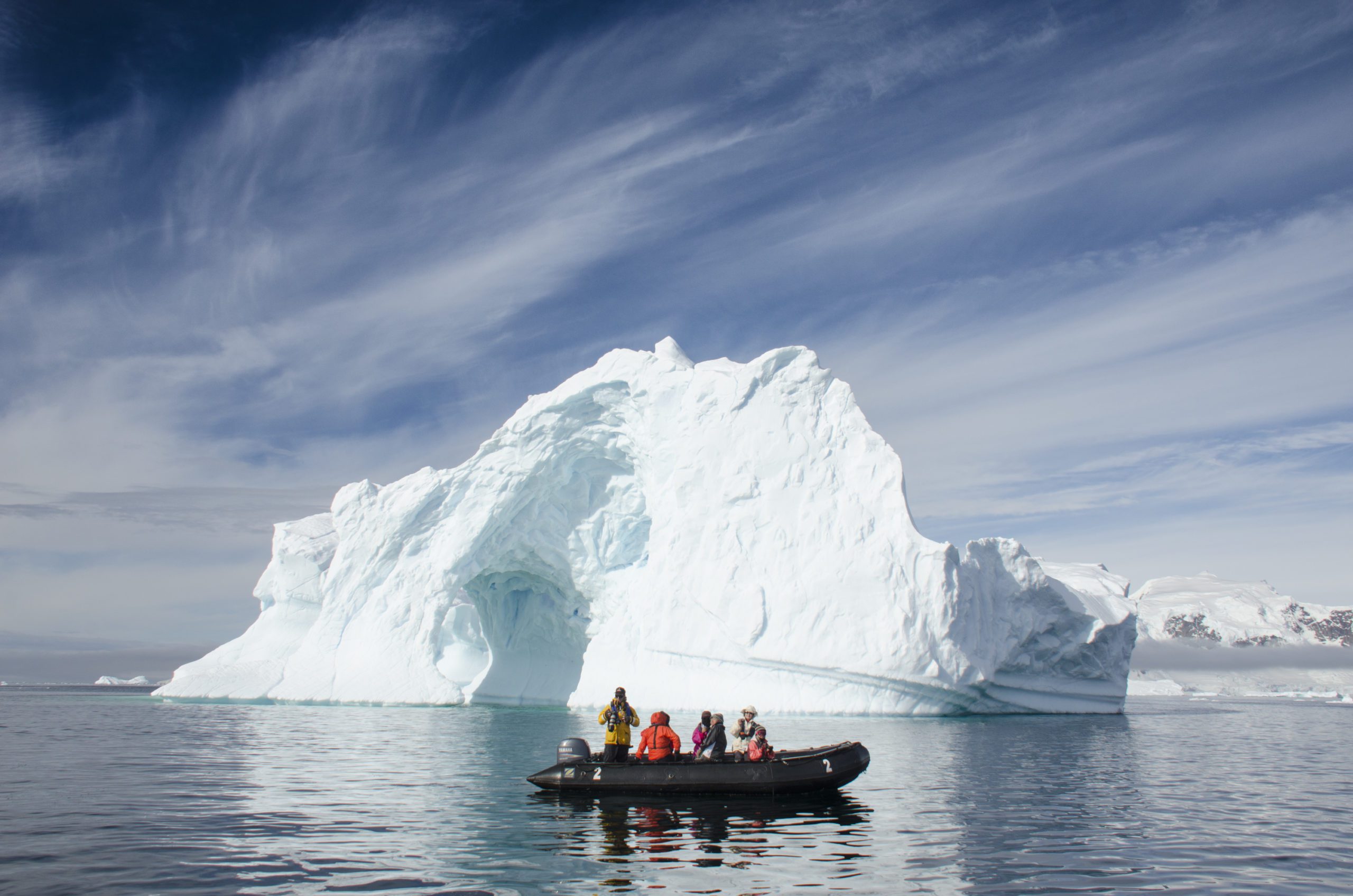 zodiac boat of guests floating in front of an iceberg in the waters of Antarctica: Luxury & Private Safaris