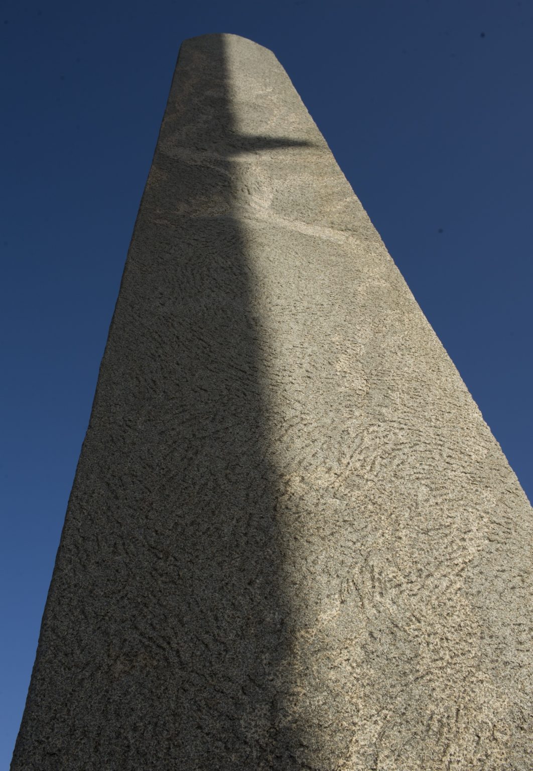 looking up at a tall standing stele with the clear blue sky in the background in Axum, Ethiopia