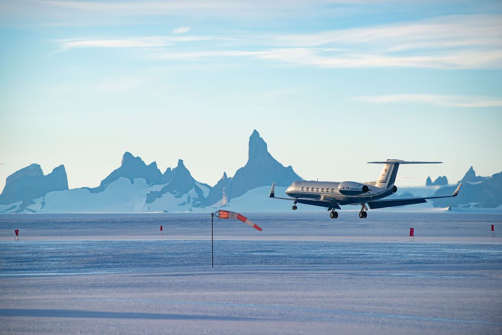Gulfstream jet landing on the ice runway in Antarctica with jagged mountain peaks in the distance
