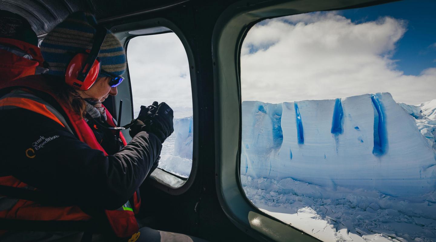 helicopter passenger taking a photo through the window of tabular icebergs in Antarctica