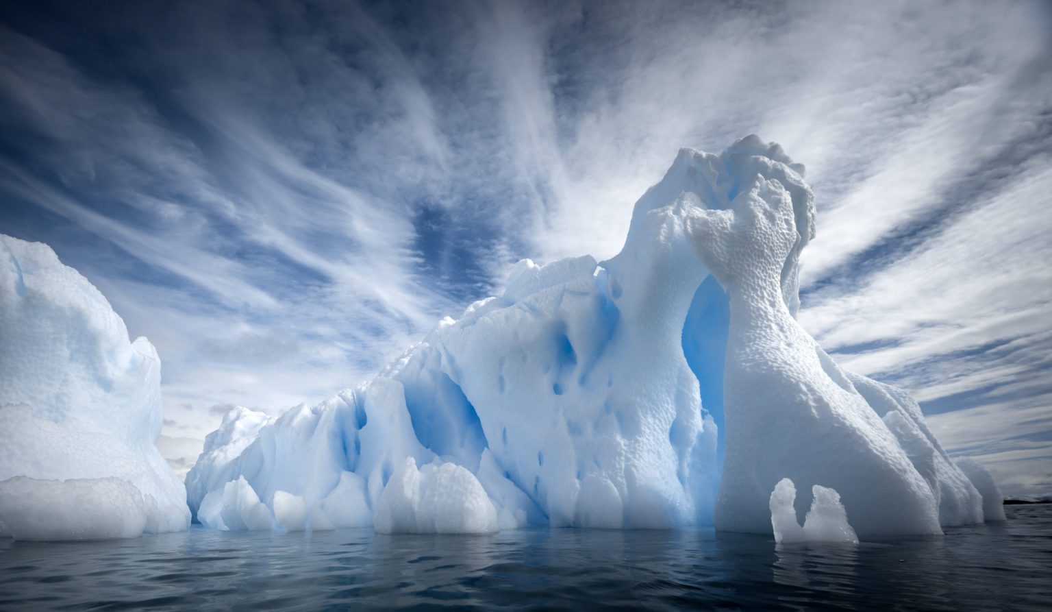 artistically carved aquamarine iceberg with white clouds above in Antarctica