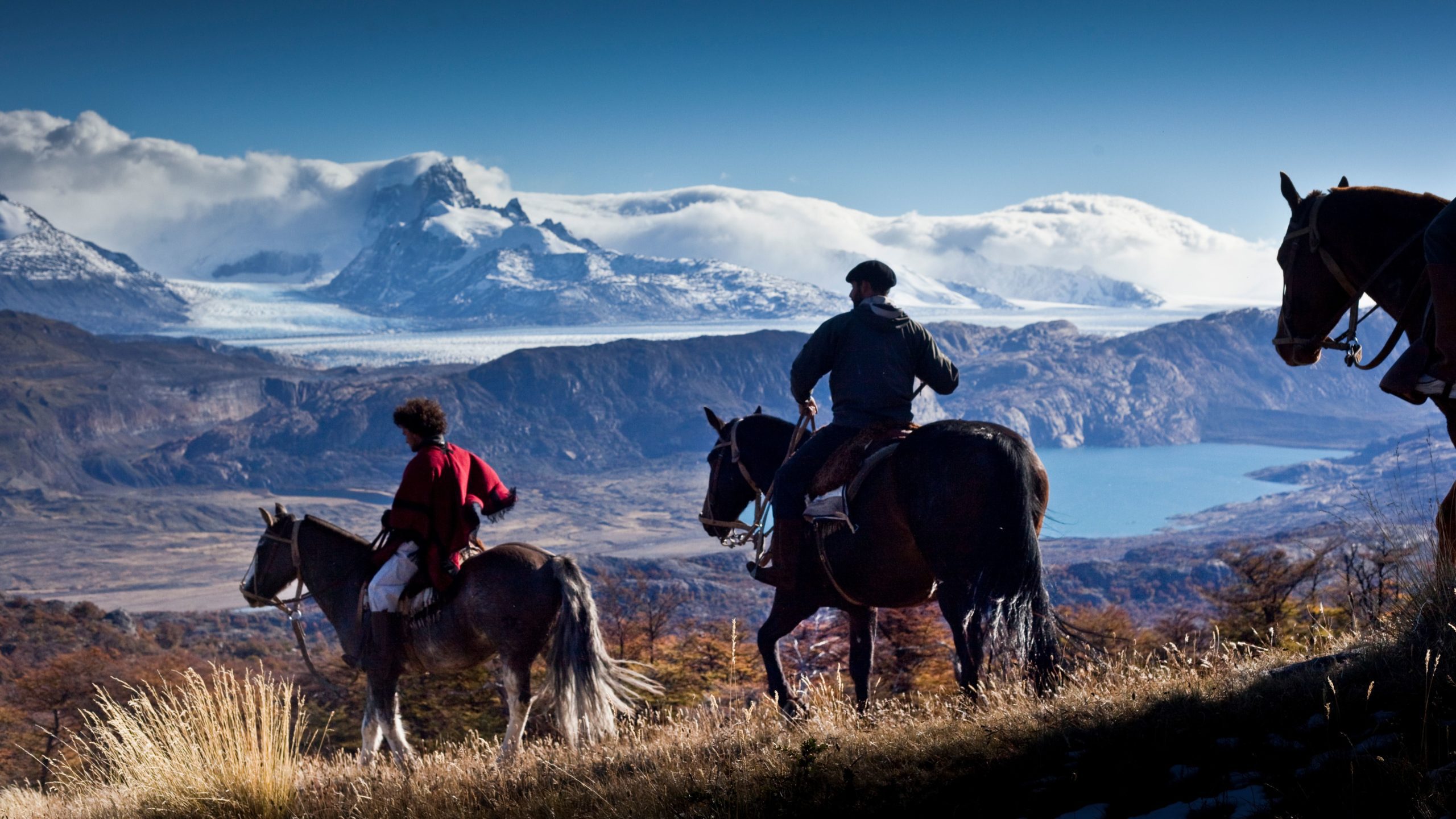 3 horses and 2 gauchos on trail overlooking lake, ice fields and mountains