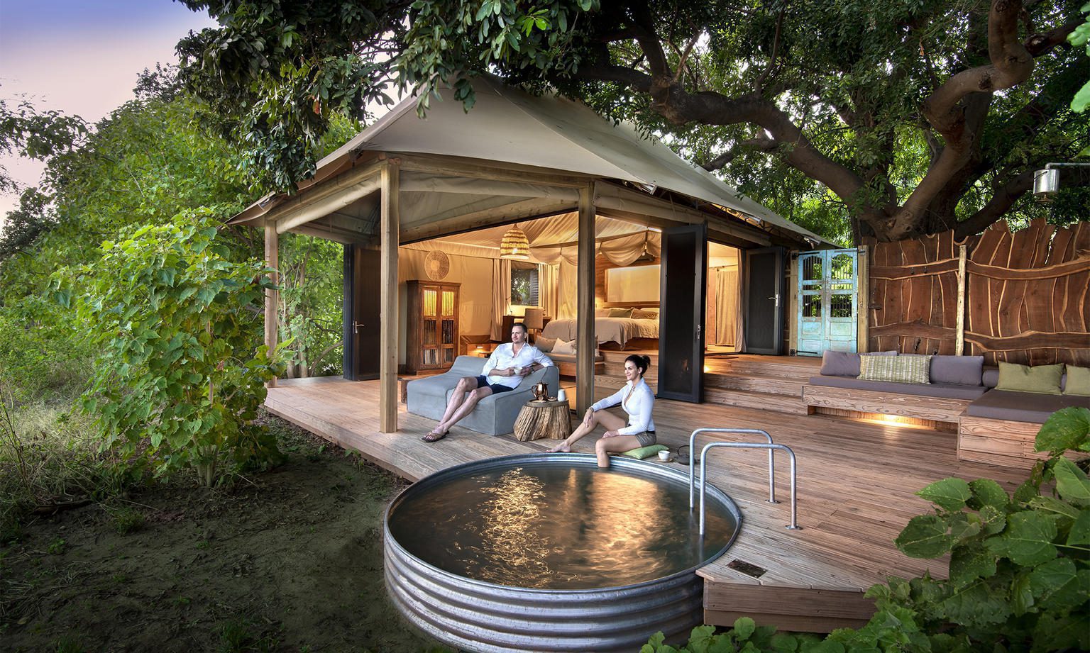 African Bushcamps, plunge pool at nyamatusi with people sitting around it on the deck of their tent on luxury safari