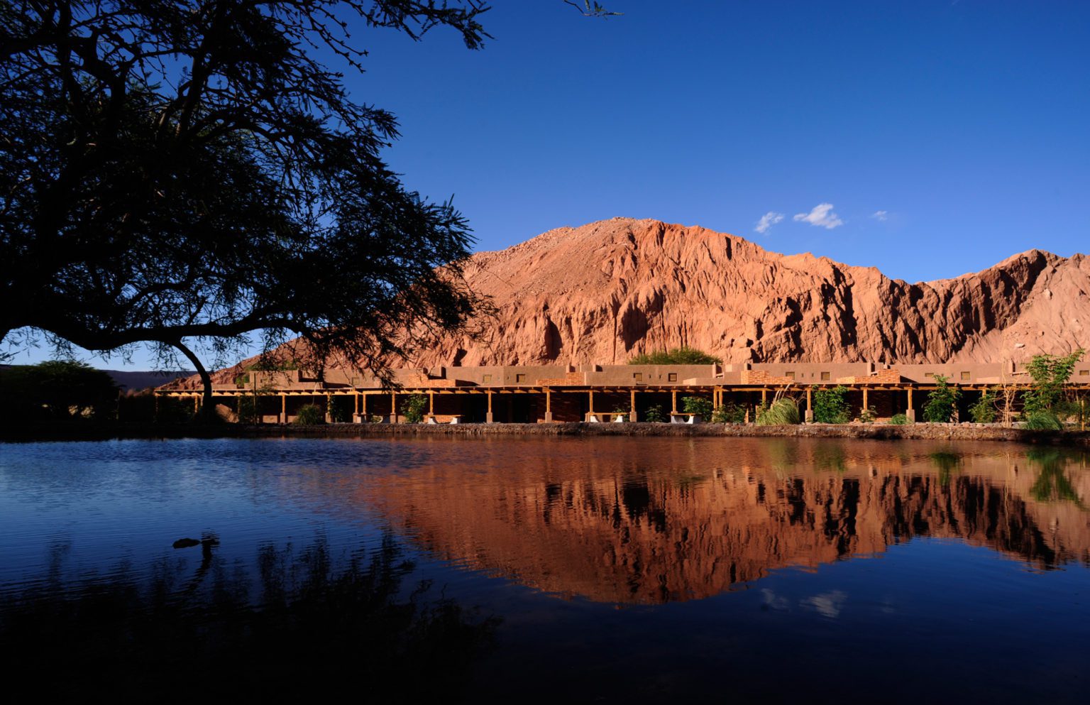 view of a lodge across water with red mountains behind