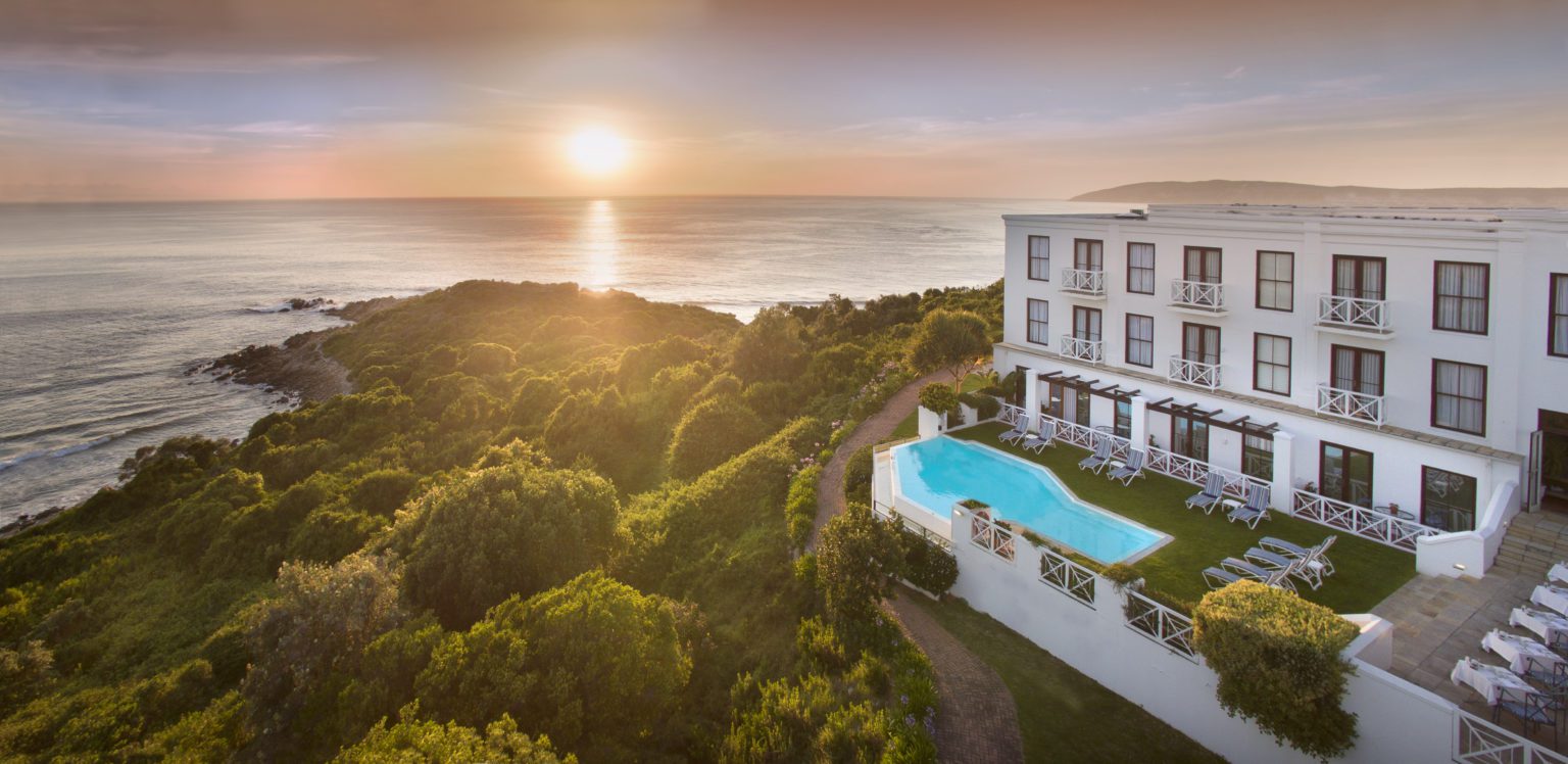 the plettenberg exterior view overlooking ocean views, lush green trees and a pretty sunset