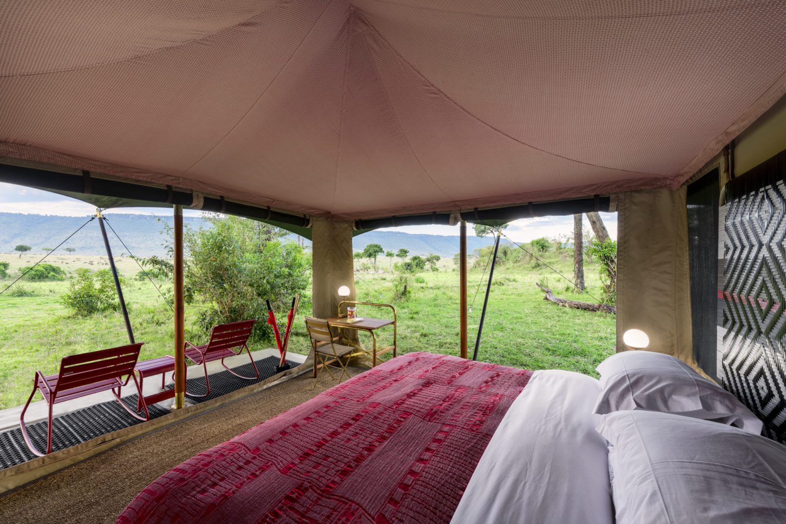 interior of a safari tent with a red blanket on the bed and open canvas sides with views into the bush.