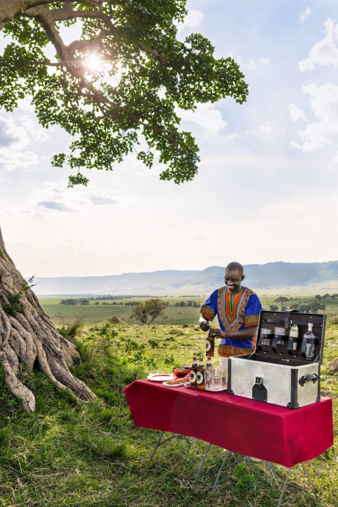 Maasai bartender with a luxury bar setup in the bush beneath a tree