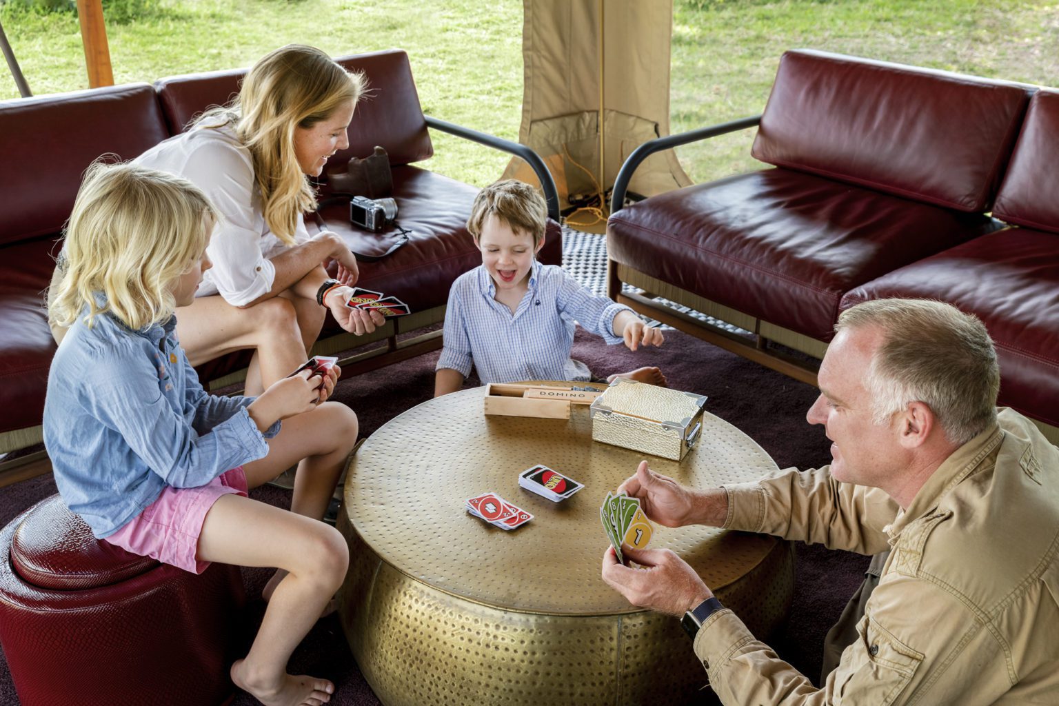 Mom and grandad play card game with kids in the lounge of a safari tent in the Maasai Mara