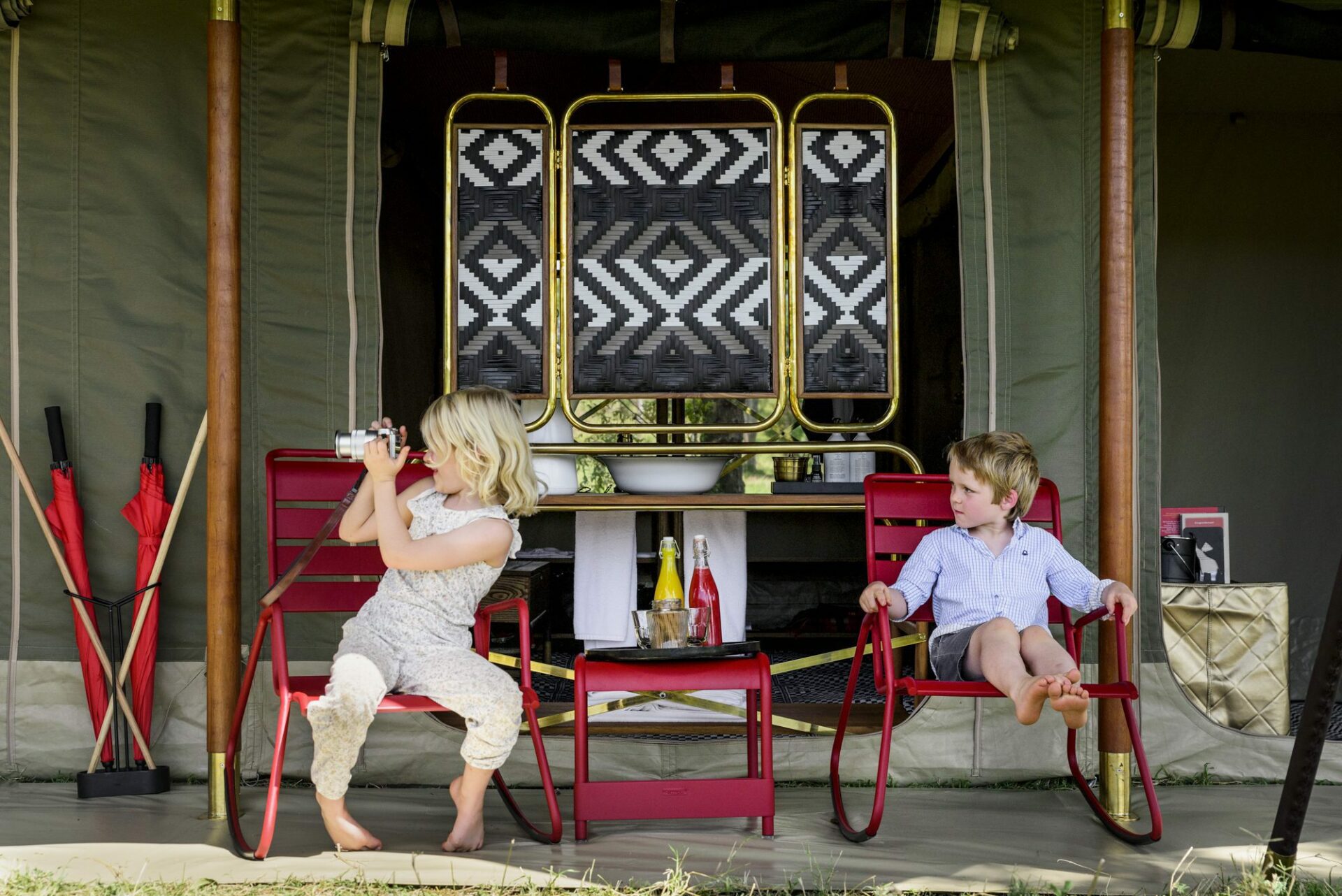 two blonde children sitting on red chairs at Angama Safari Camp looking at something in the distance