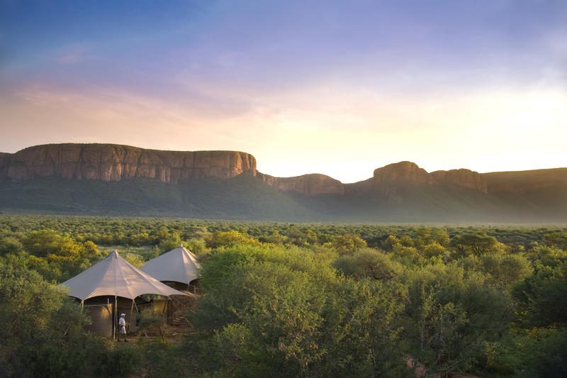 luxury safari tents nestled in the bush with mountains in the background at sunrise