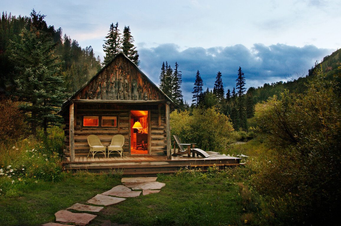 single cabin lit from within against a mountainous landscape