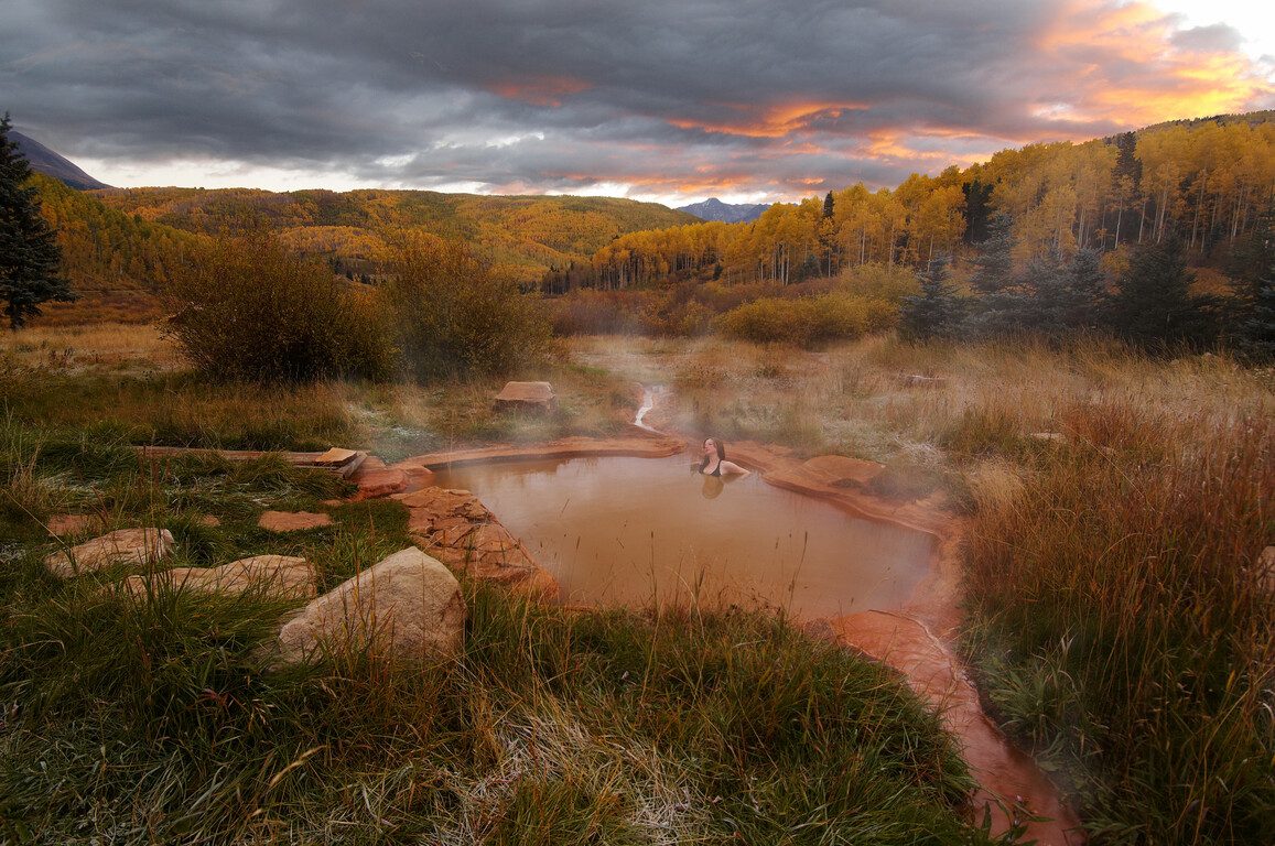 woman soaking in a natural hot spring at sunrise with the mountains in the background
