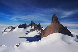 massive brown monolith rocks emerge from the snow against a blue sky in Antarctica