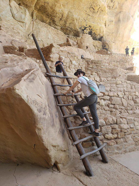 man and boy climbing a wooden ladder at bandelier national monument