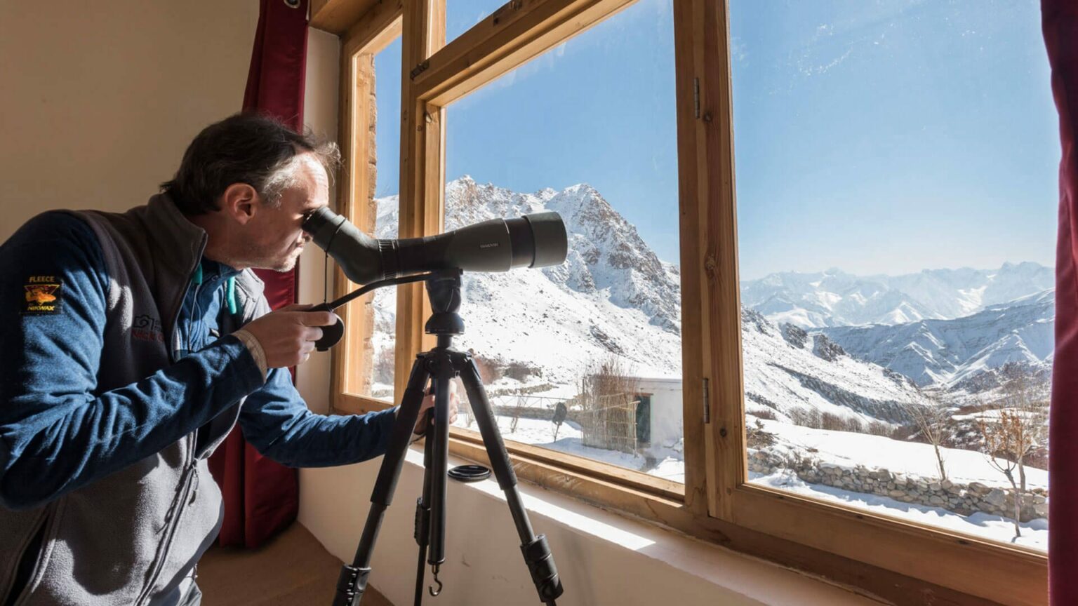 person looking out of a telescope into the Himalayas from a room at Snow Leopard Lodge